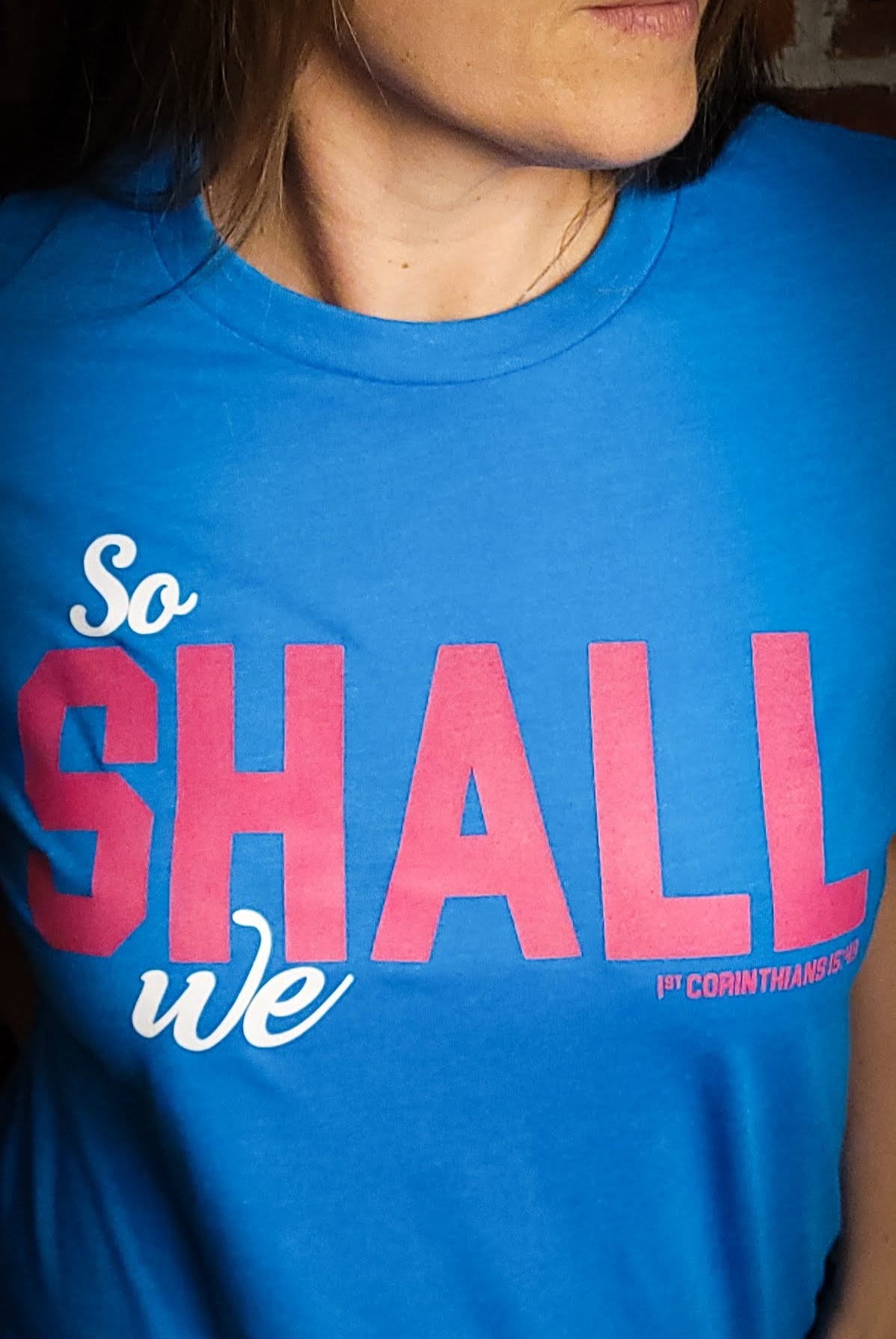 Teal blue shirt with the words So shall we across the front. The verse mentioned with 1 Corinthians