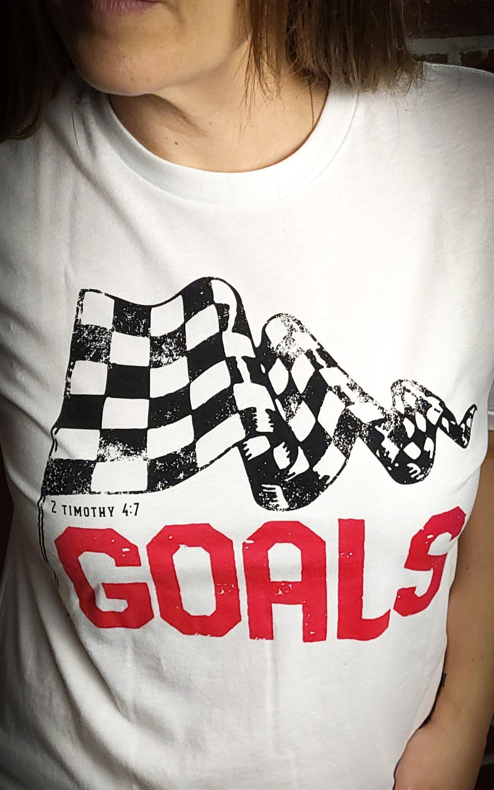 White T-shirt with the word Goals across the front underneath a checkered flag. The verse 2 Timothy 4:7