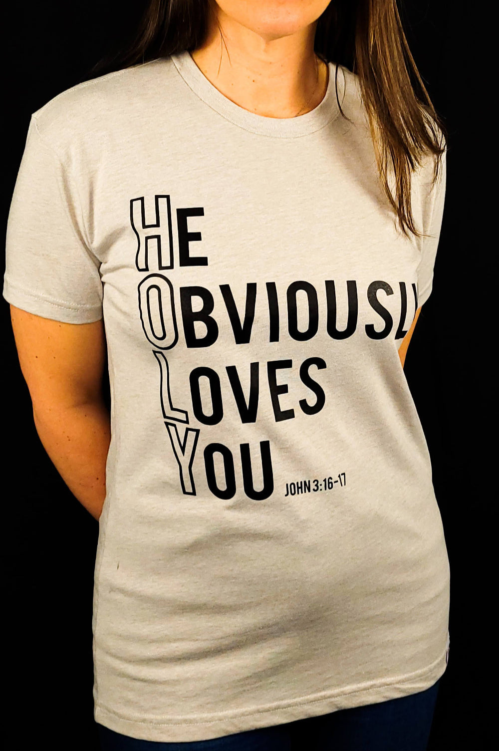 Beige t-shirt with the words He Obviously Loves You written downwards to show the word HOLY. The verse points to John 3:16-17
