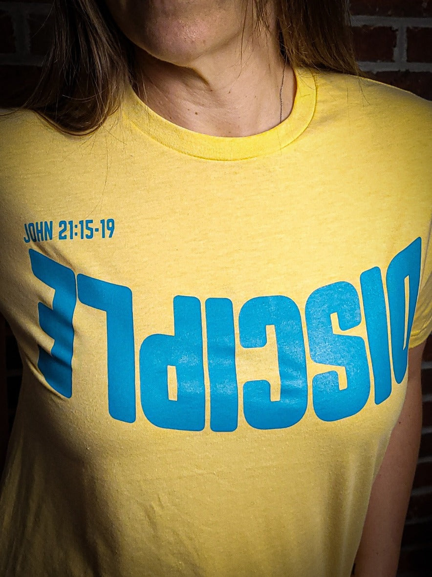 Yellow shirt with the Word Disciple upside down on it. The verse is pointing to John 21:15-19.