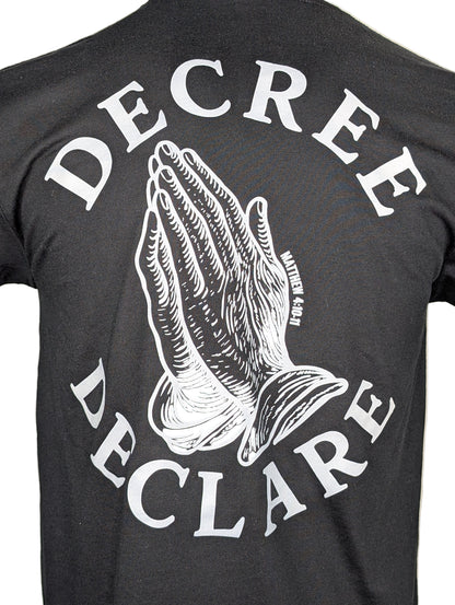 Black t-shirt with white praying hands graphic and text 'DECREE DECLARE' on a beige background
