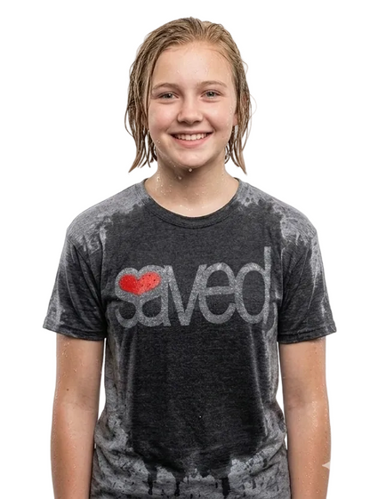 A smiling young woman with wet hair wearing a dark gray mineral-wash t-shirt with a red heart and the word 'saved' printed on the front, set against a plain white background.
