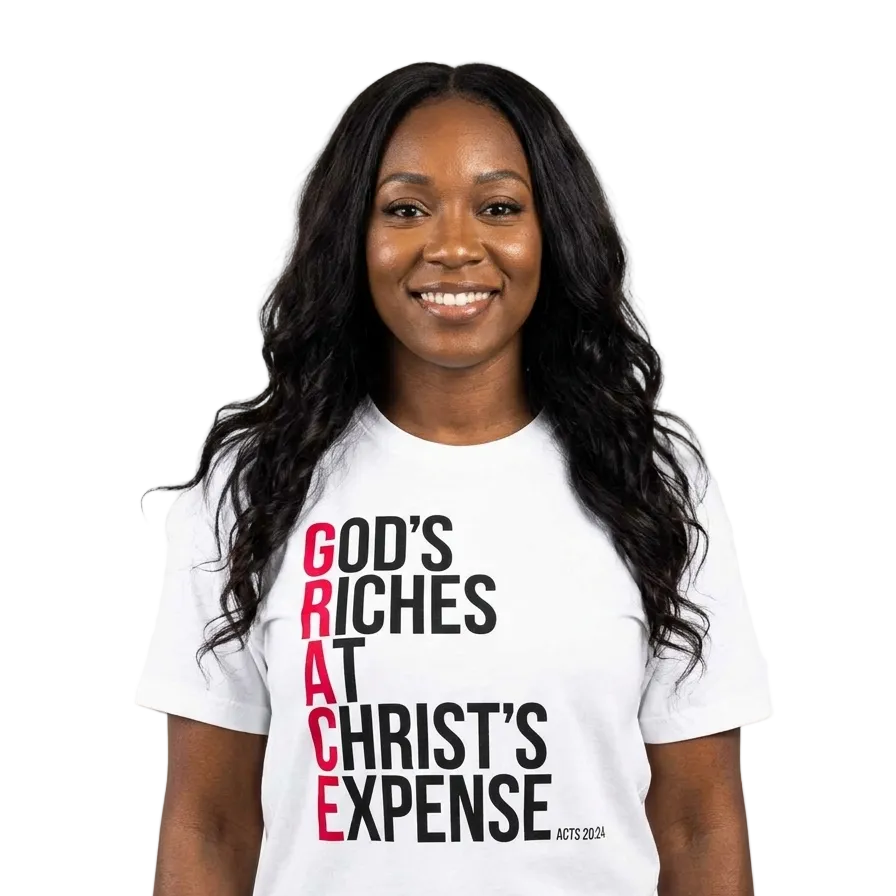 A smiling woman with long black hair wearing a white graphic t-shirt. The shirt features the text 'GOD'S RICHES AT CHRIST'S EXPENSE' printed vertically on the front, with 'GOD'S' and 'AT' in black, 'CHRIST'S' in red, and 'EXPENSE' in black, along with 'ACTS 2:34' in small black text.