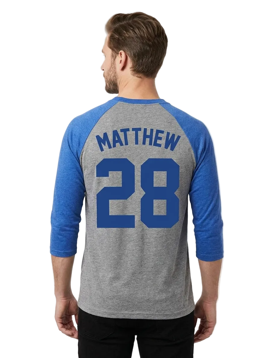 A man viewed from the back wearing a heather gray and blue raglan baseball t-shirt with 'MATTHEW' and the number '28' printed in blue on the back.