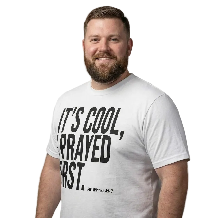 A man wearing a white graphic t-shirt with black text that reads 'IT'S COOL, PRAYED FIRST. PHILIPPIANS 4:6-7' on a solid gray background.