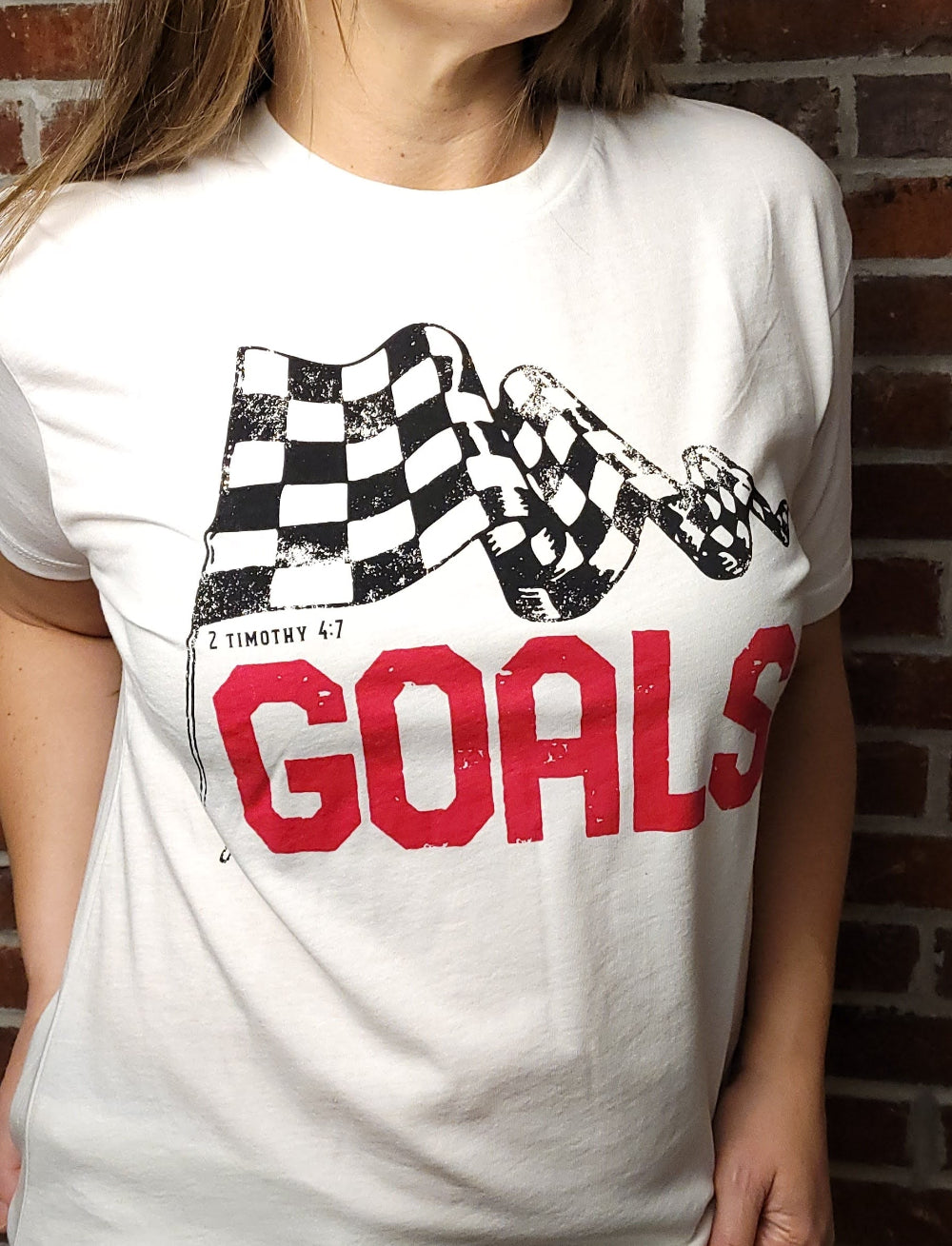 White T-shirt with the word Goals across the front underneath a checkered flag. The verse 2 Timothy 4:7 