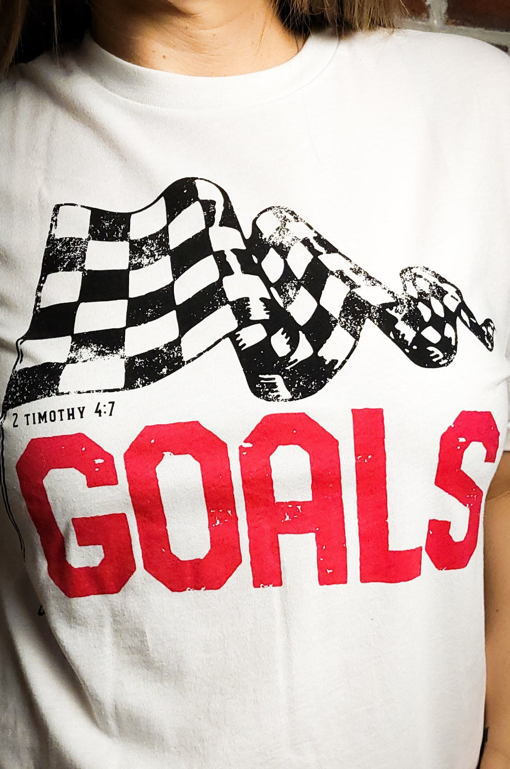 White T-shirt with the word Goals across the front underneath a checkered flag. The verse 2 Timothy 4:7 