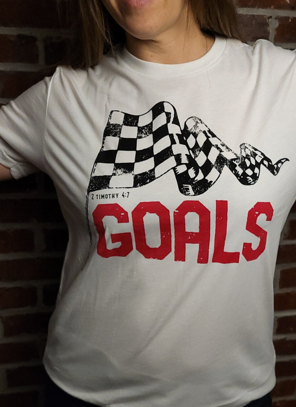 White T-shirt with the word Goals across the front underneath a checkered flag. The verse 2 Timothy 4:7 