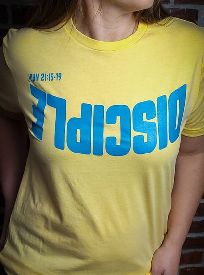 Yellow shirt with the Word Disciple upside down on it. The verse is pointing to John 21:15-19.