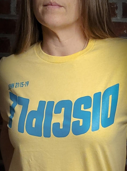 Yellow shirt with the Word Disciple upside down on it. The verse is pointing to John 21:15-19.